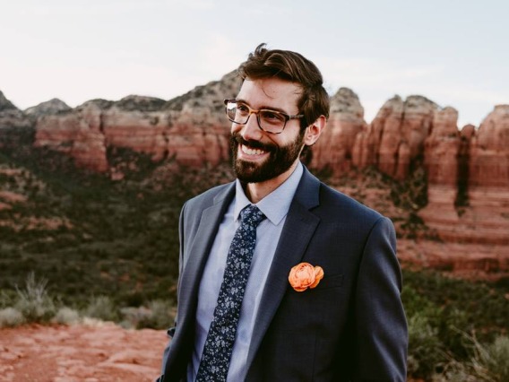 Peter Scorcia smiling for photo, wearing dark grey suite jacket with flower in pocket, red rock formations in background