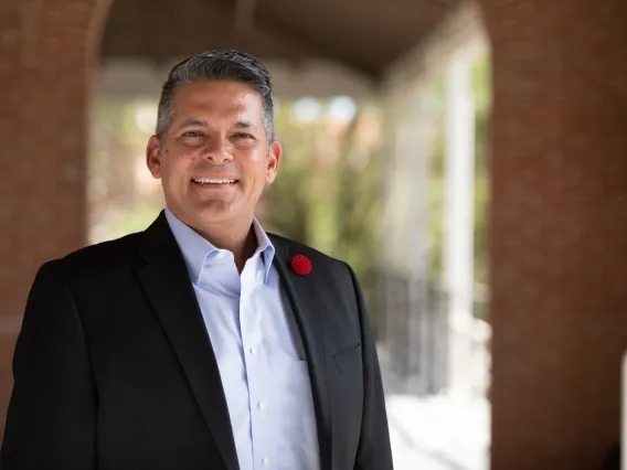 Rafael Meza smiling for photo, wearing light blue button up and black suit jacket with red pin