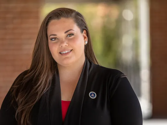 Jessica Salata smiling for photo, wearing red blouse, black suite jacket, and UArizona pin