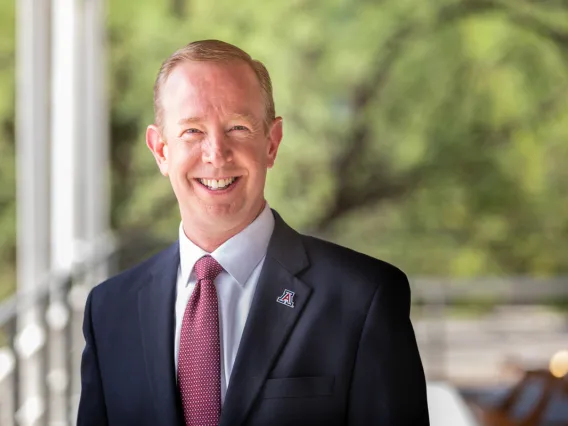Art Young smiling for photo, wearing dark suite, white shirt, and red tie with UArizona pin