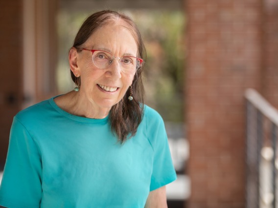 Ellen Fishman smiling for photo, wearing teal blouse and earnings, and red rimmed glasses
