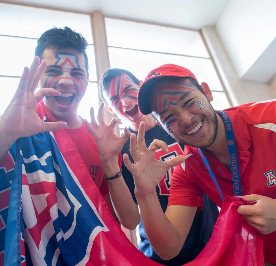 Three students posing for photo, dressed in UArizona apparel for sports event