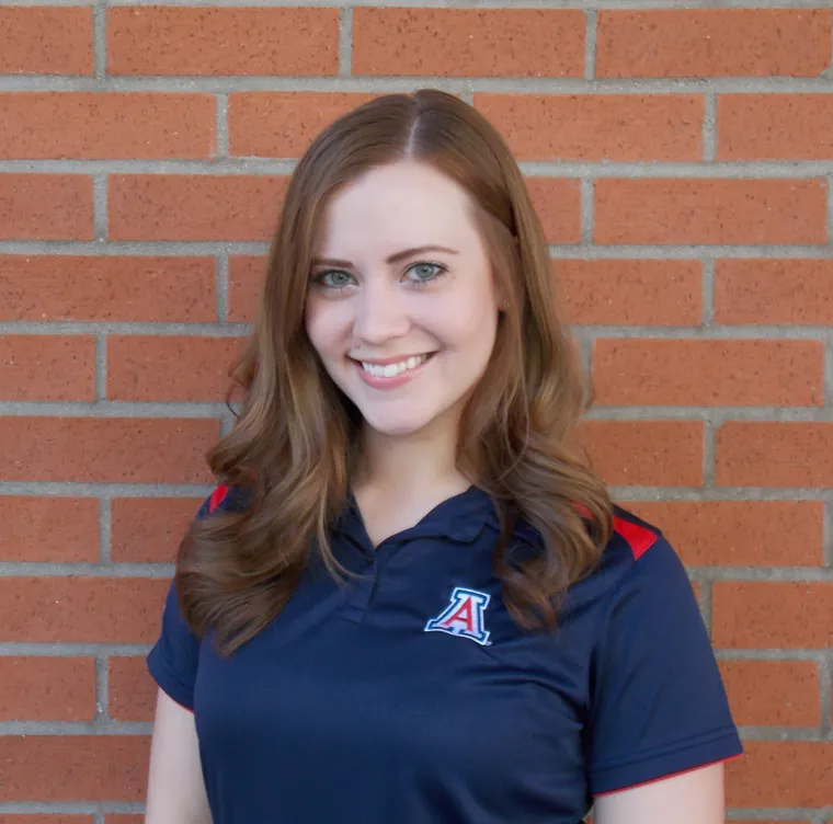 Danielle Crosby smiling for photo, wearing blue UA polo, brick wall in background