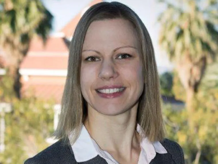 Helen Horetski smiling for photo, wearing white collared shirt, palm trees in background