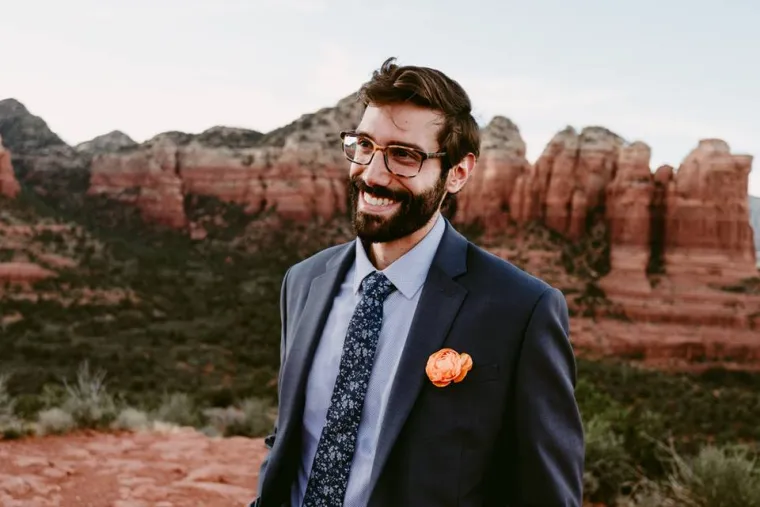 Peter Scorcia smiling for photo, wearing dark grey suite jacket with flower in pocket, red rock formations in background