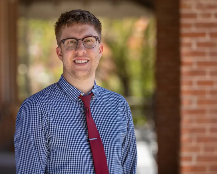 Dan Kellish smiling for photo, wearing blue button up shirt and red tie