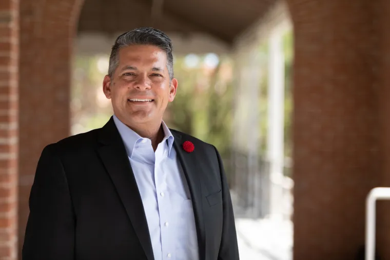 Rafael Meza smiling for photo, wearing light blue button up and black suit jacket with red pin