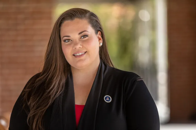 Jessica Salata smiling for photo, wearing red blouse, black suite jacket, and UArizona pin