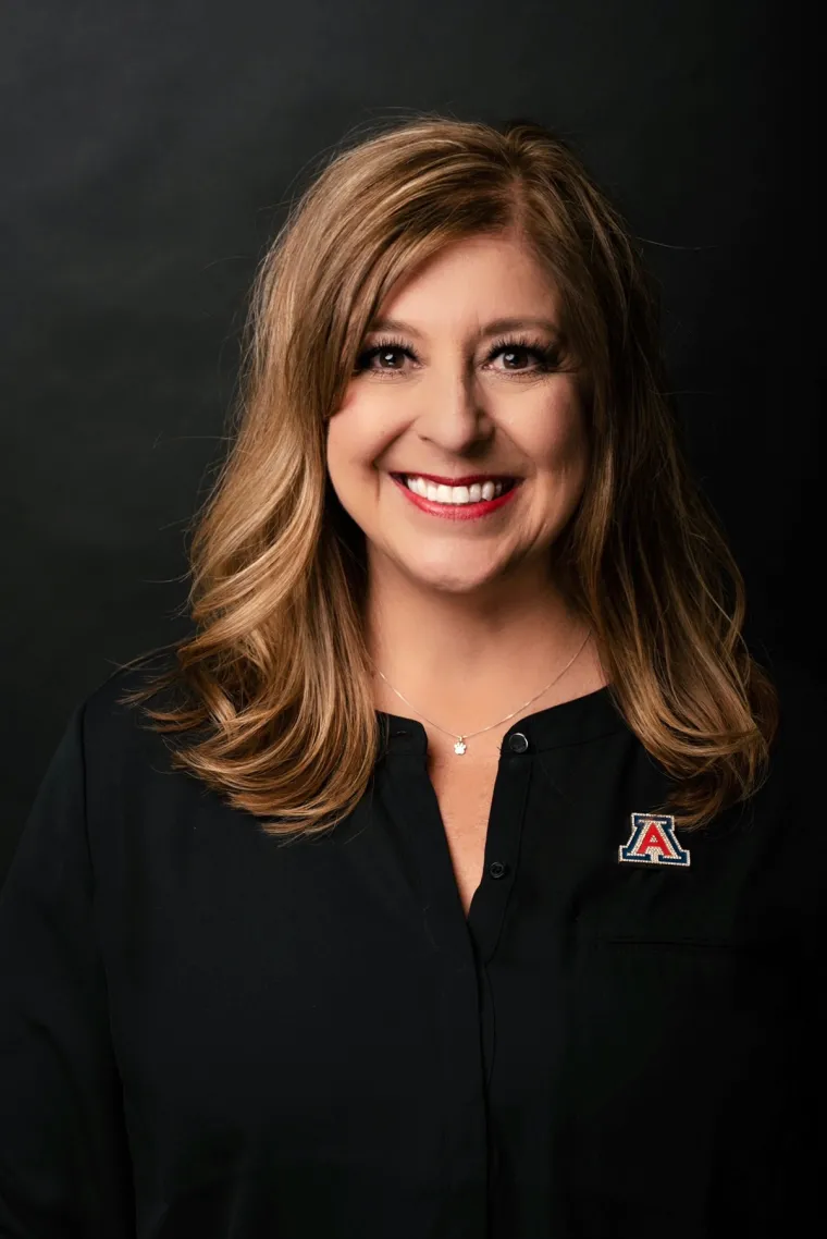 Kasey Urquidez smiling for photo, wearing black blouse and UArizona pin