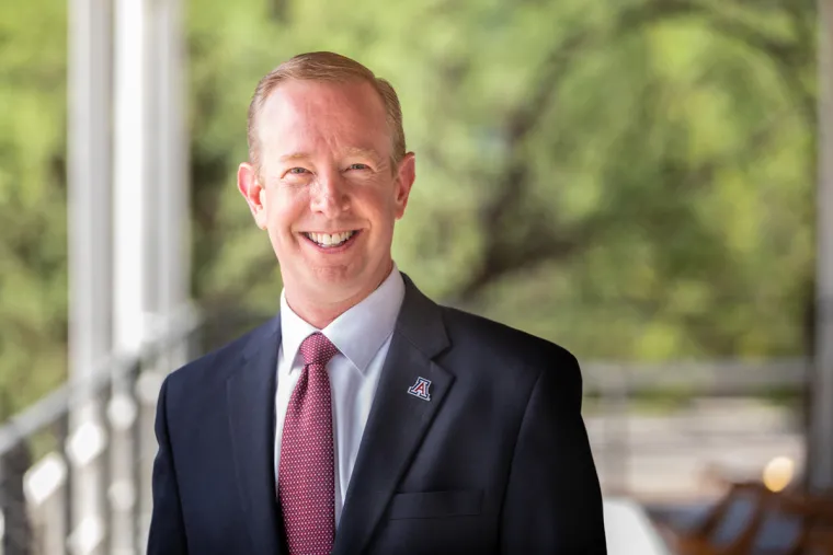 Art Young smiling for photo, wearing dark suite, white shirt, and red tie with UArizona pin