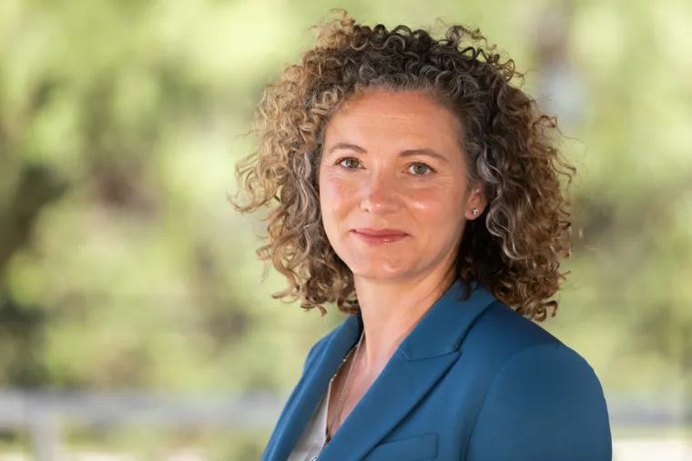 Abra McAndrew smiling lightly for photo, wearing light blue suit jacket