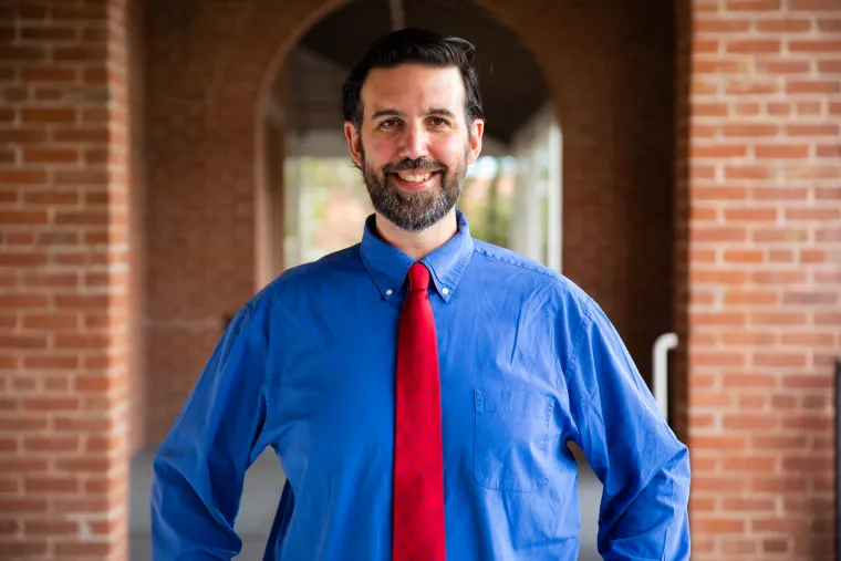 Joe smiling while wearing a blue shirt and red tie